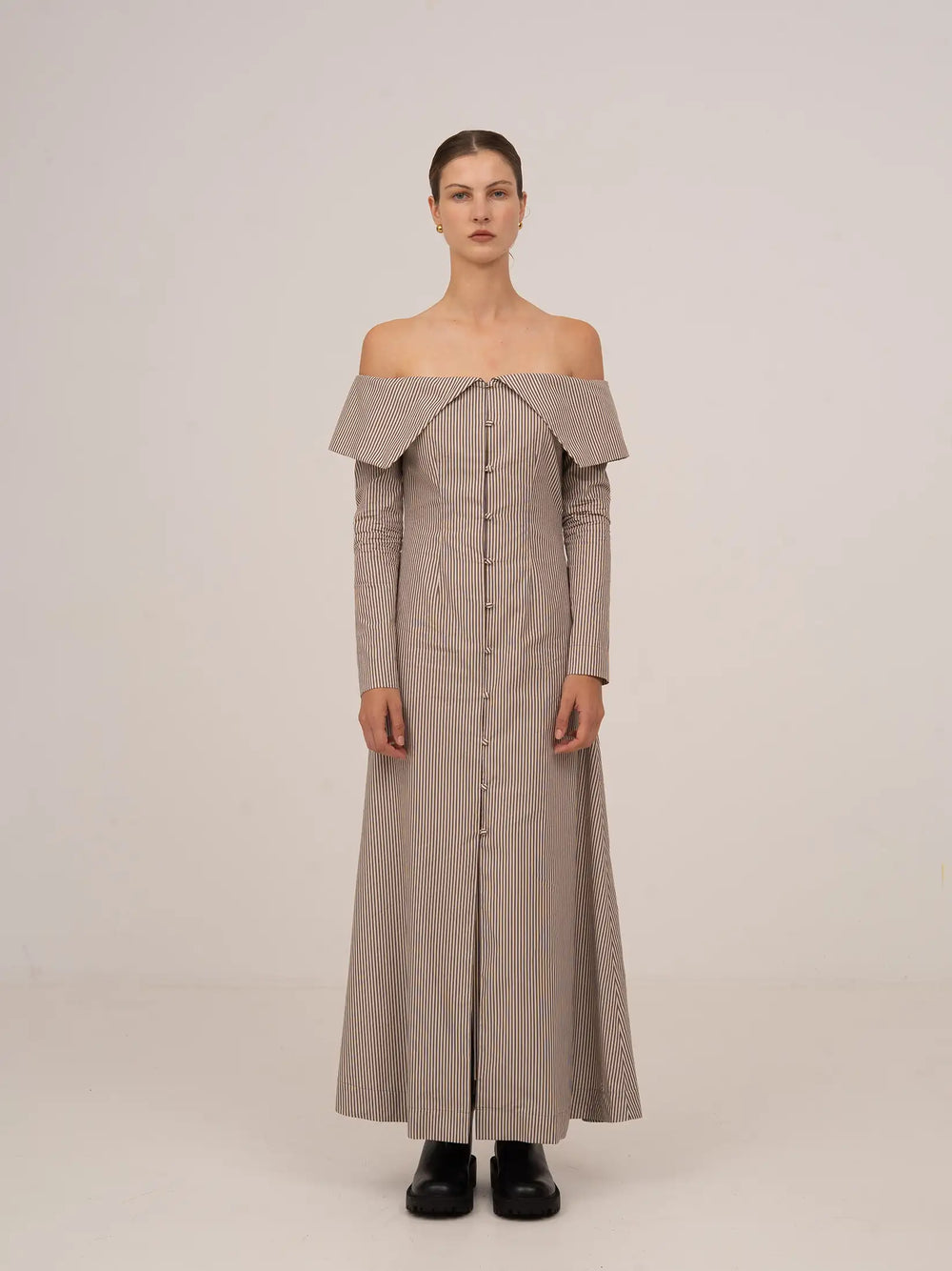 Vestido largo de rayas en tonos marrón y beige, con escote bardot off-shoulder, manga larga ajustada y silueta recta de caída fluida.