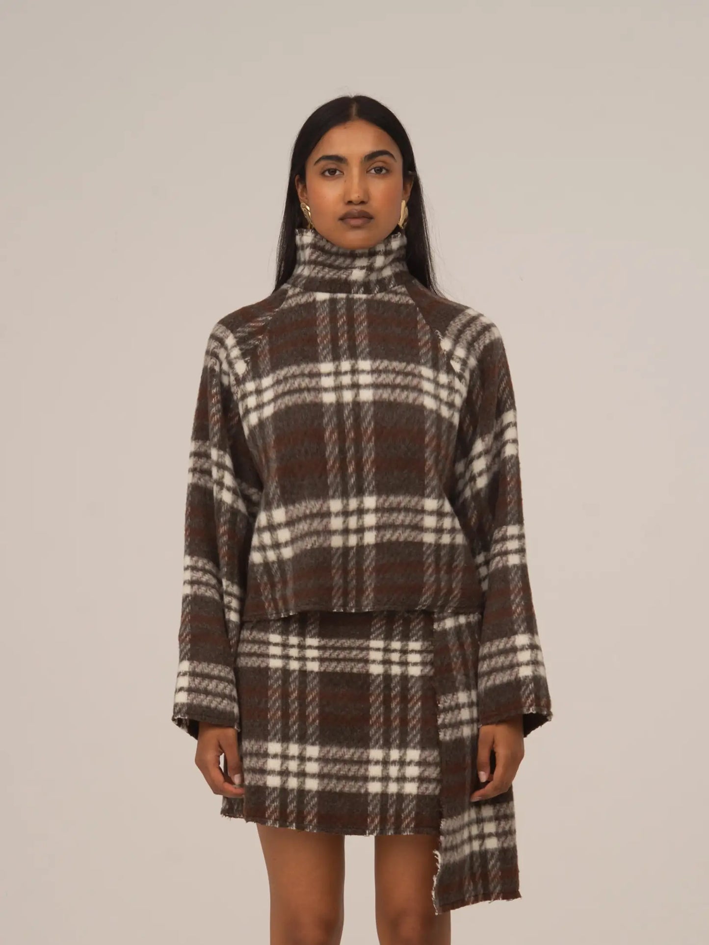 Top de cuello alto con estampado de cuadros marrón y blanco, de manga larga y corte recto, combinado con falda a juego, presentado sobre modelo en estudio con fondo neutro.