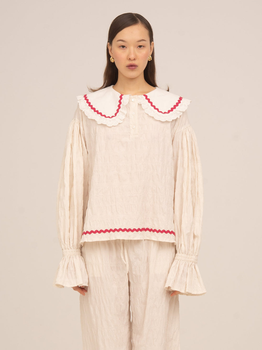 Blusa de pijama color crema de Carmen Says con cuello amplio y volante en contraste rojo, manga larga con puño fruncido y diseño romántico ideal para looks de descanso con estilo.