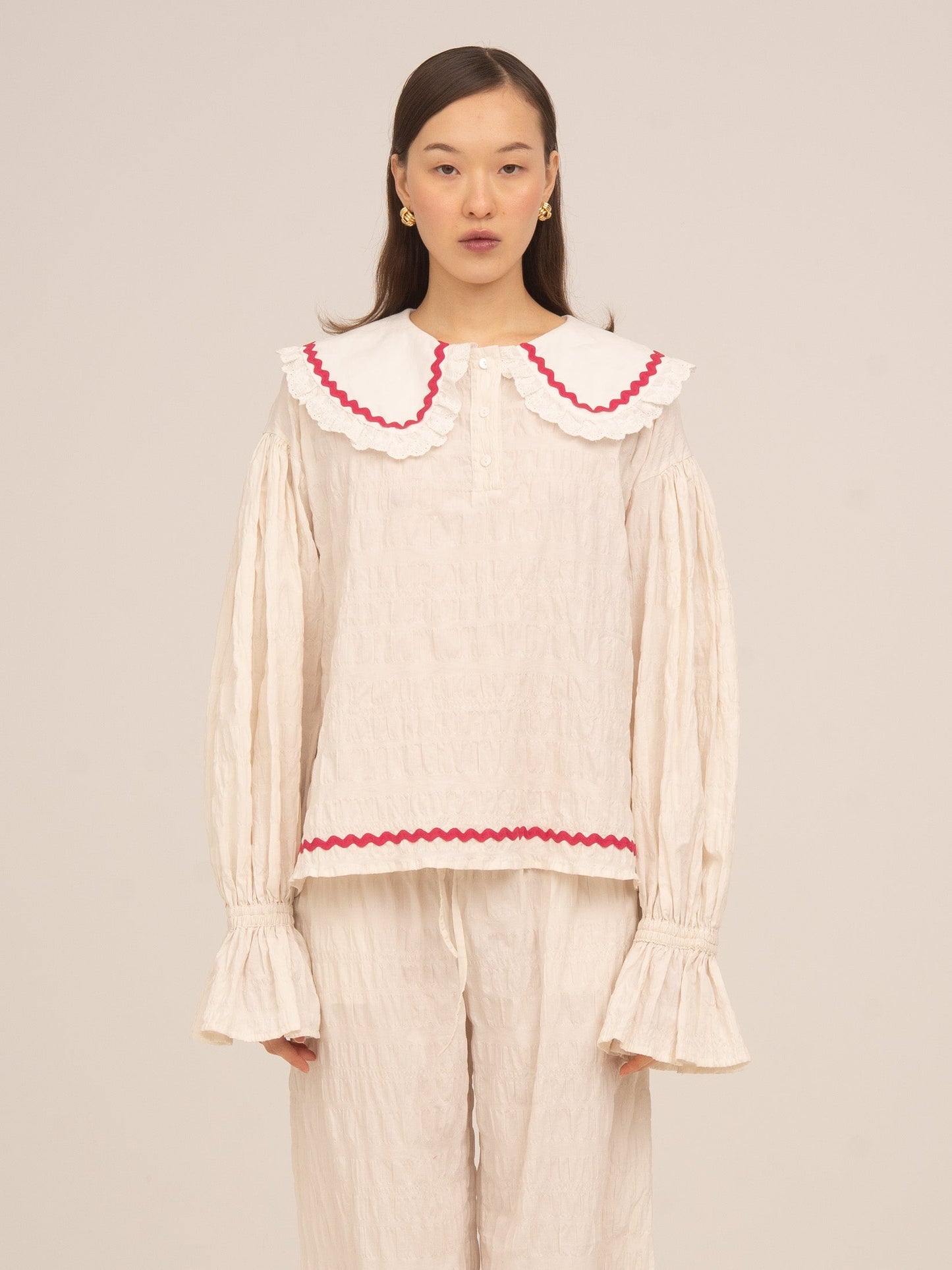 Blusa de pijama color crema de Carmen Says con cuello amplio y volante en contraste rojo, manga larga con puño fruncido y diseño romántico ideal para looks de descanso con estilo.