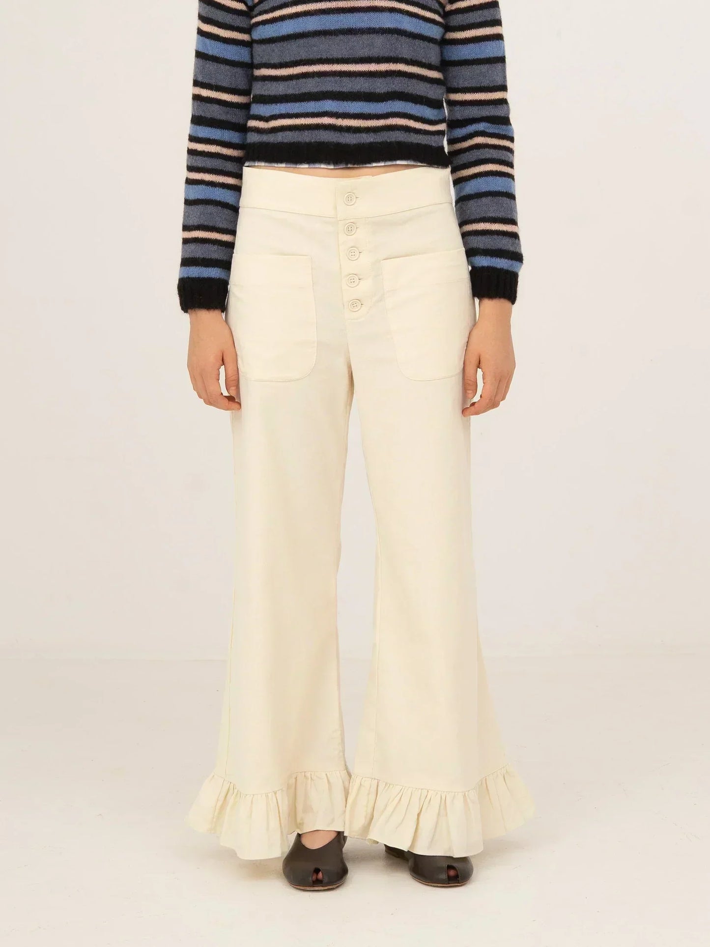 Pantalón blanco de pana con corte recto y pernera ligeramente acampanada, cierre frontal con botones y bajo con volante, presentado sobre modelo en estudio con fondo neutro.