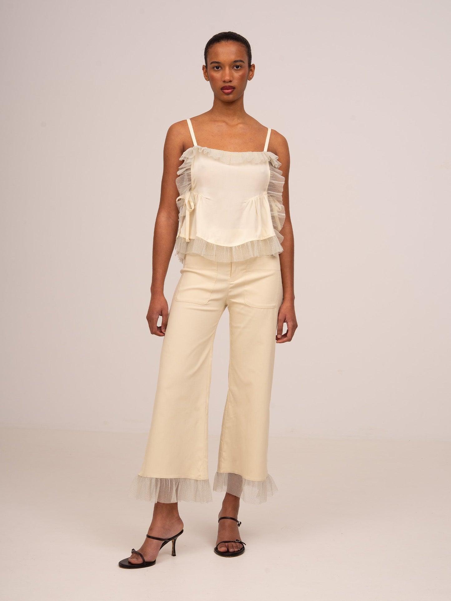 Conjunto de top crema de tirantes con volantes y lazadas laterales y pantalón crema de pierna ancha con bajo de volante.