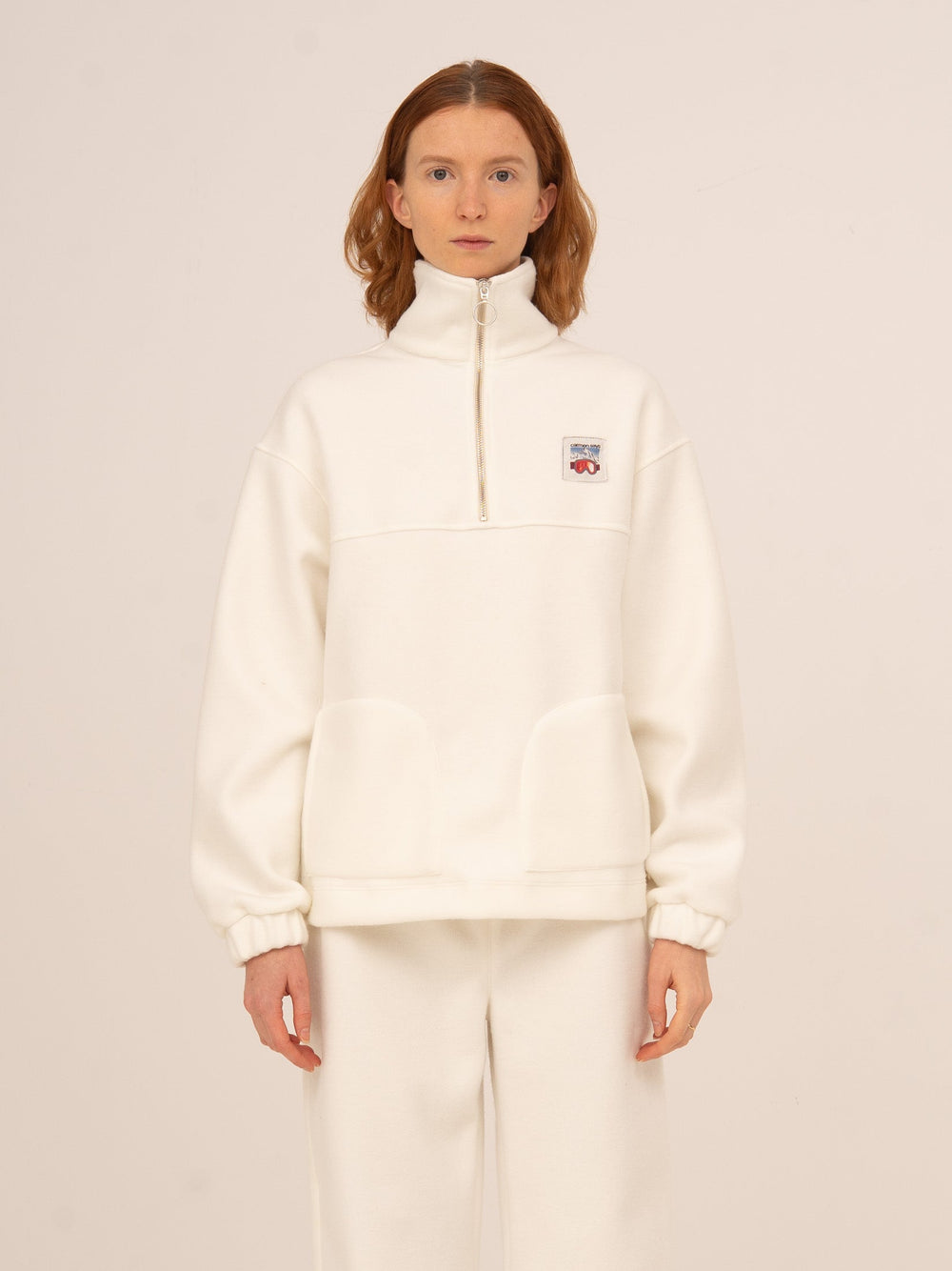Sudadera femenina en color blanco con cuello alto y media cremallera, tejido suave tipo polar y corte relajado, ideal para looks cómodos y elegantes de invierno, après-ski o estilo casual urbano.