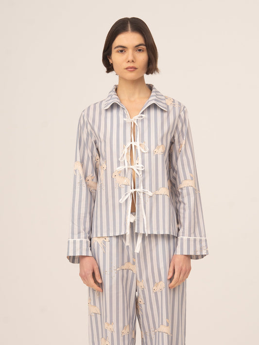 Modelo femenina vistiendo camisa de pijama en tonos azul claro con rayas verticales y estampado de ciervos en color beige, conjunto de inspiración loungewear, fotografiada de frente sobre fondo neutro.