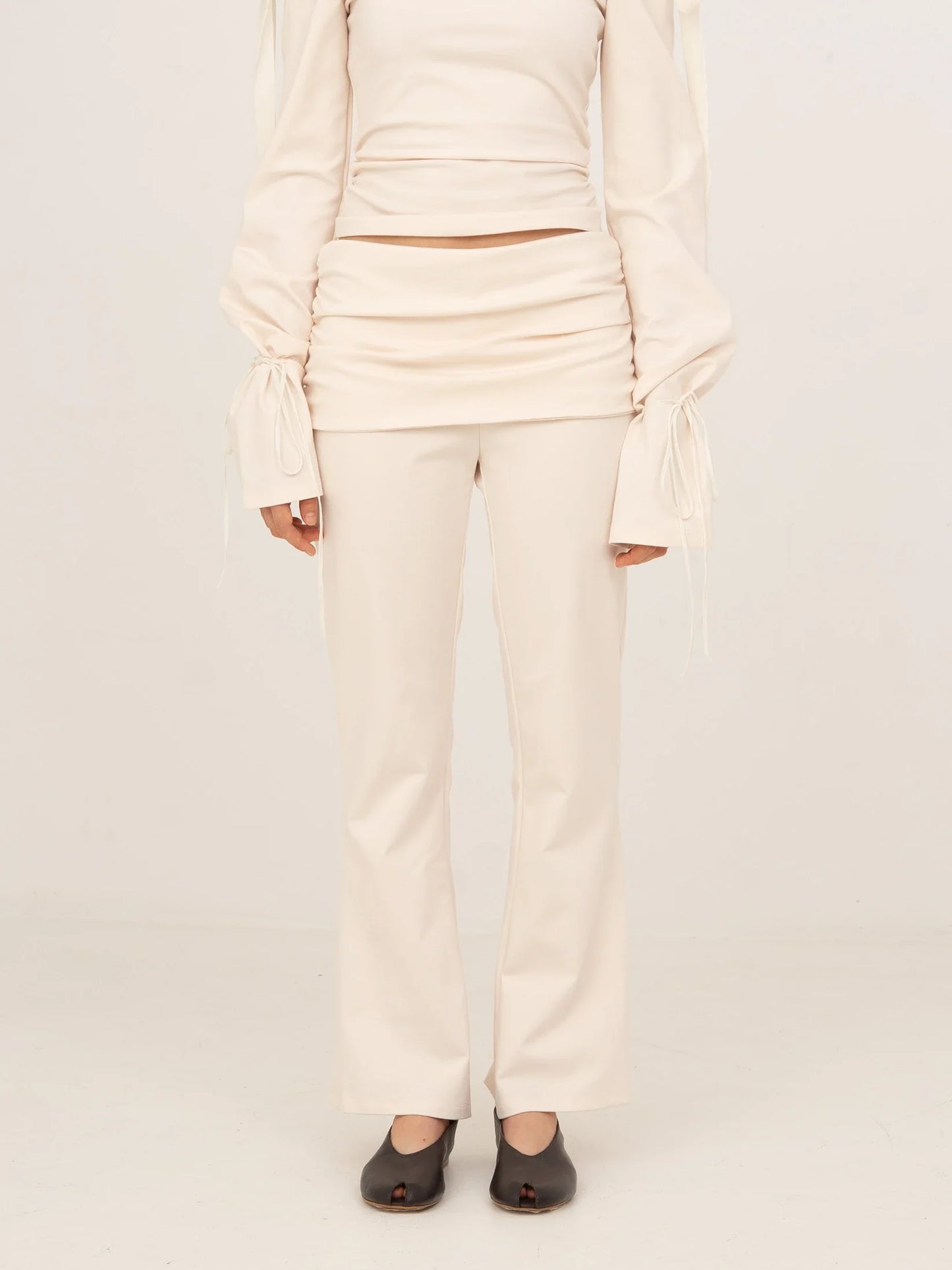 Pantalón blanco de tejido jersey con corte recto y silueta estilizada, cintura lisa y caída suave, presentado sobre modelo en estudio con fondo neutro.