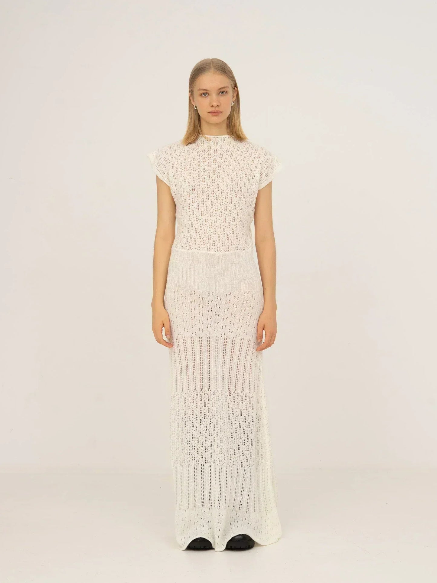 Vestido maxi blanco de punto calado con diseño de textura abierta, cuello alto, manga corta y silueta recta de caída ligera, presentado sobre modelo en estudio con fondo neutro.