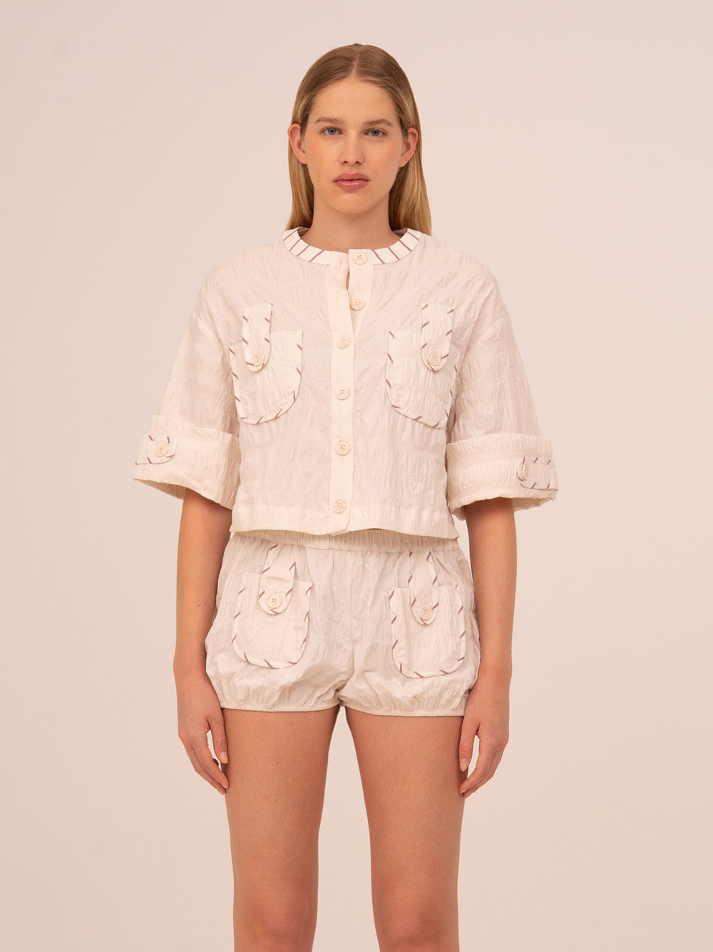 Camisa cropped blanca de mujer con diseño minimalista y corte moderno. Confeccionada en tejido ligero, presenta cierre frontal y silueta corta ideal para combinar con prendas de talle alto. Una camisa versátil y atemporal perfecta para looks casuales o elegantes de verano.