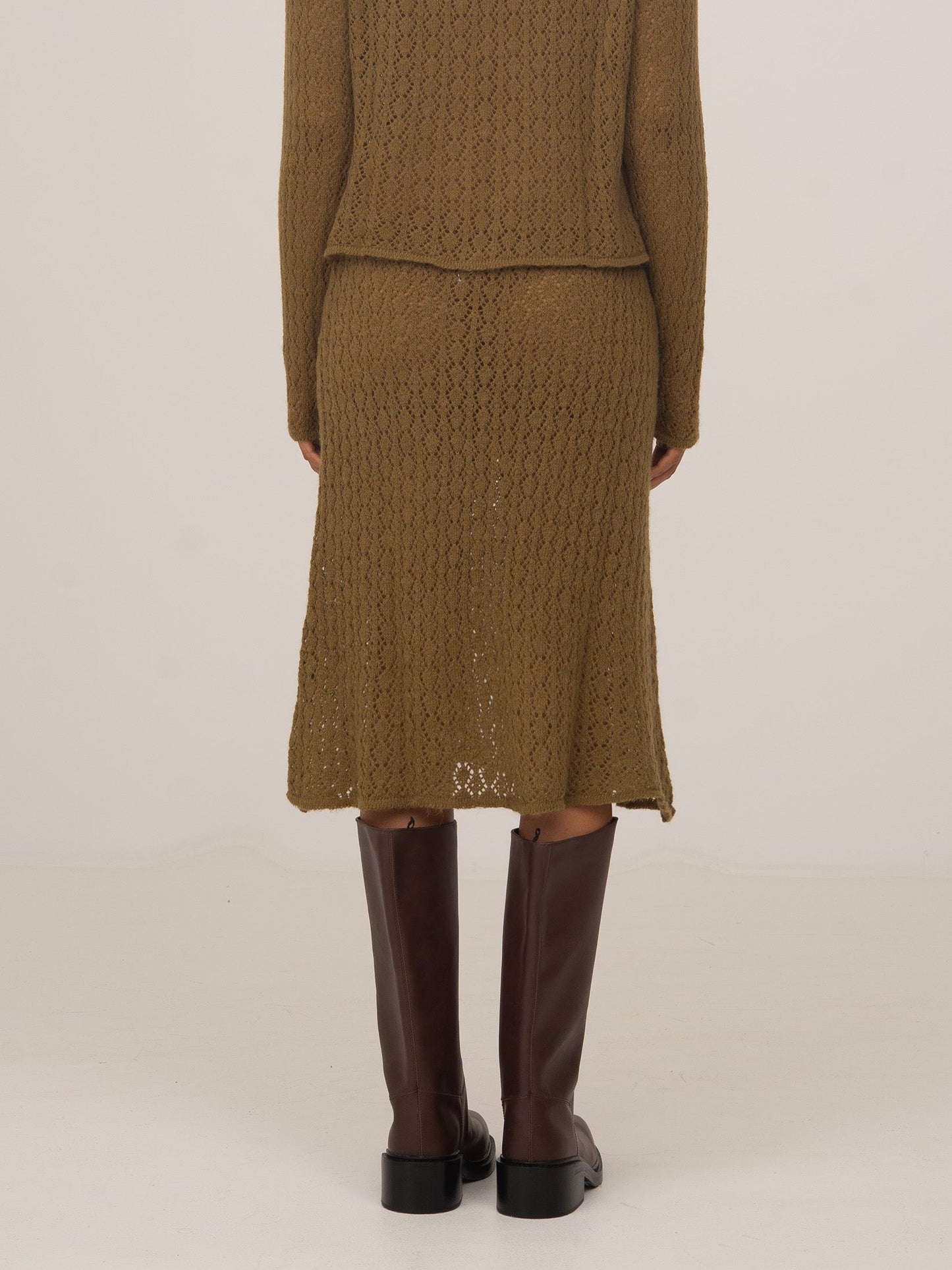 Vista trasera de falda midi de punto verde con textura trenzada, combinada con botas altas marrones