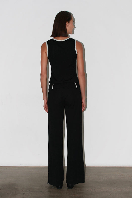 Three-quarter front view – elegant black pants featuring metallic button details on the waistband.