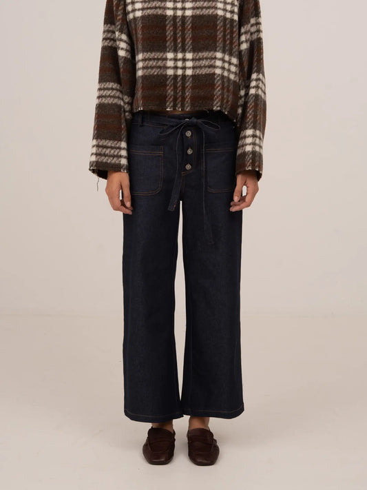 Vaquero denim azul oscuro de tiro medio y corte recto, con cierre frontal de botones, detalle de lazada en la cintura y acabado limpio, presentado sobre modelo en estudio con fondo neutro.