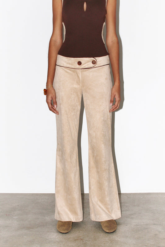  Front view of the Andrea Pants in beige suede with contrasting brown piping, featuring a low-rise fit, curved waistband, and signature front button detail.
